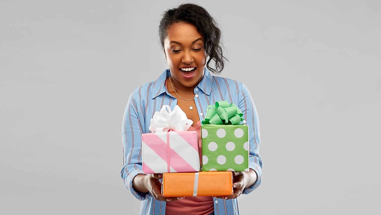Happy african american young woman with gift boxes over gray background