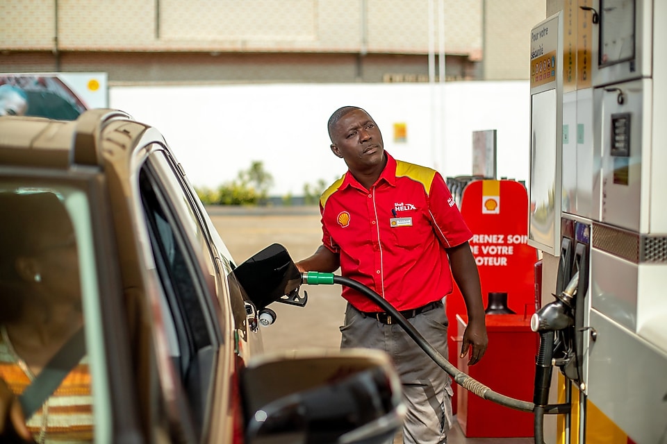 Employé Shell accueillant un automobiliste souriant sur la piste de distribution