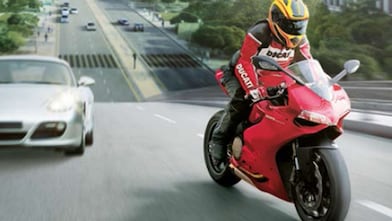 Moto rouge et conducteur sur une route avec des voitures et des bâtiments dans l&rsquo;arrière-plan.