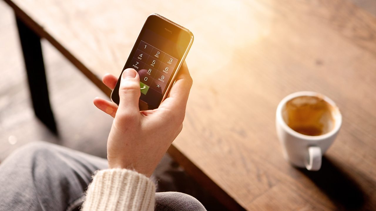 Homme tenant un téléphone portable et buvant un café
